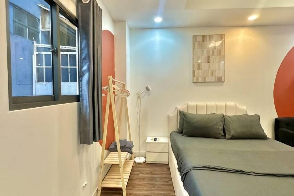 Ein Schlafzimmer mit einem Bett, einem Nachttisch, einer Lampe und einem Fenster mit Vorhängen.