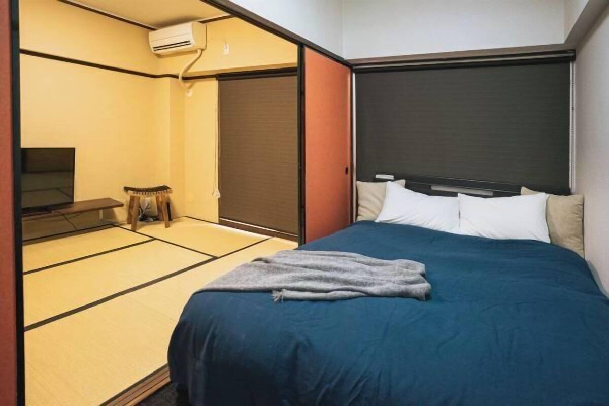 A room with tatami flooring, a bed with a dark blue bedspread, a television, and a sliding door.