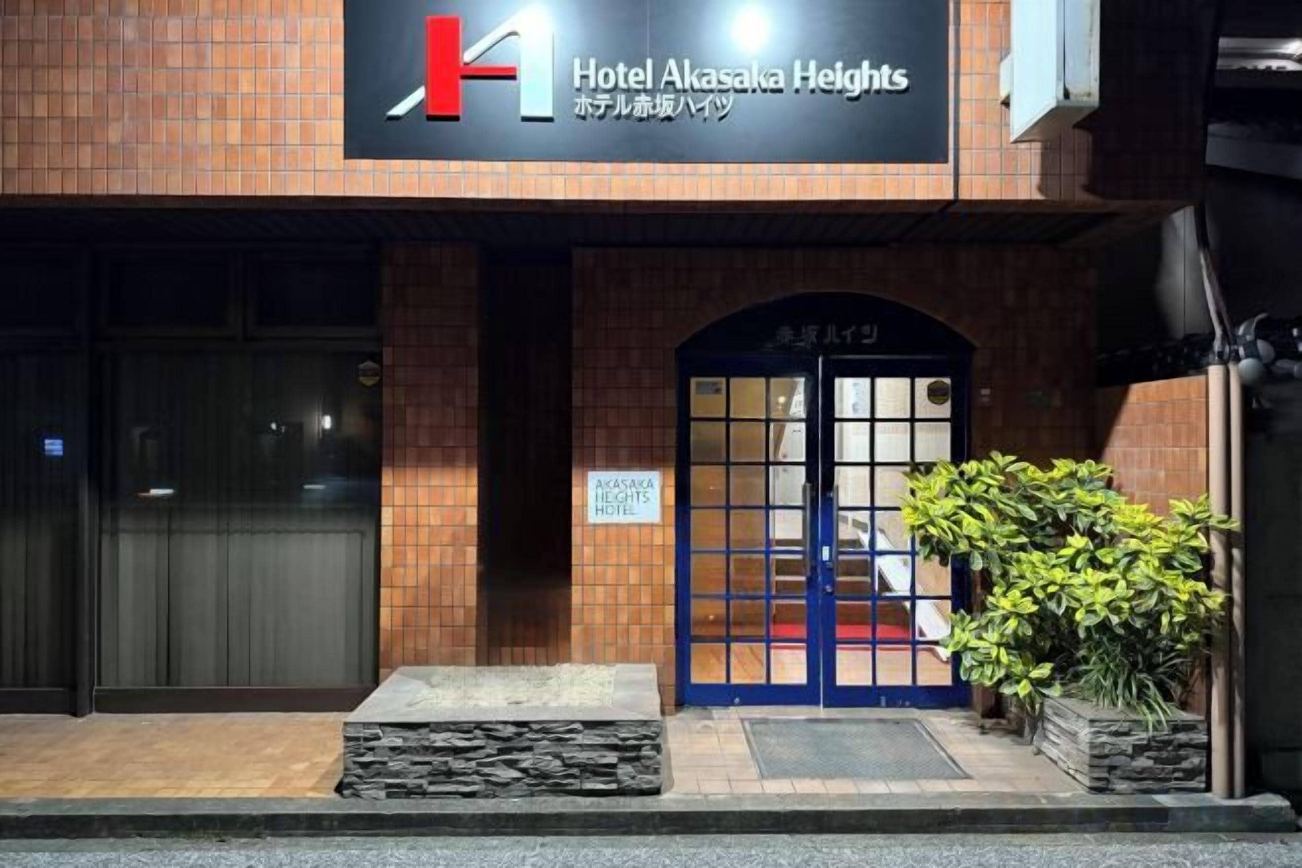 A hotel entrance with a prominent sign, a blue door, and a small step leading up to the entrance.