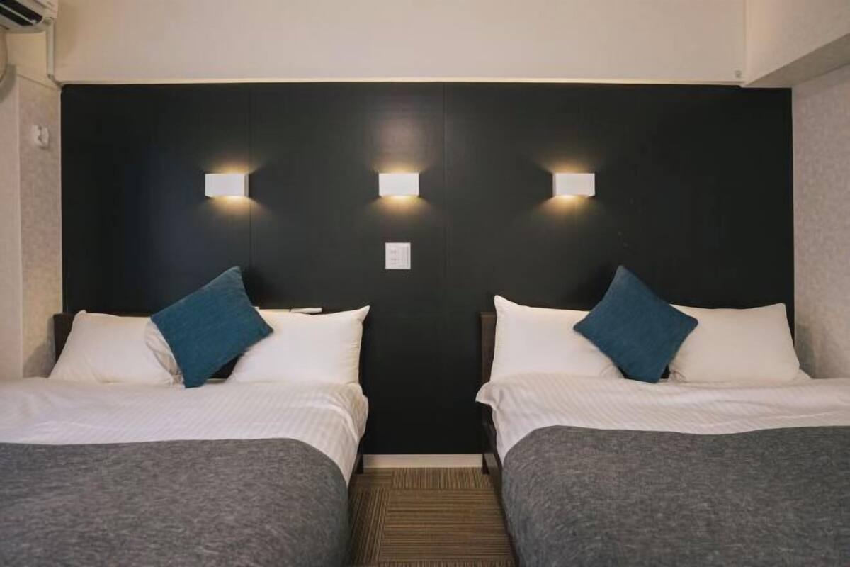 A hotel room with two beds, a dark headboard, and wall-mounted lights.