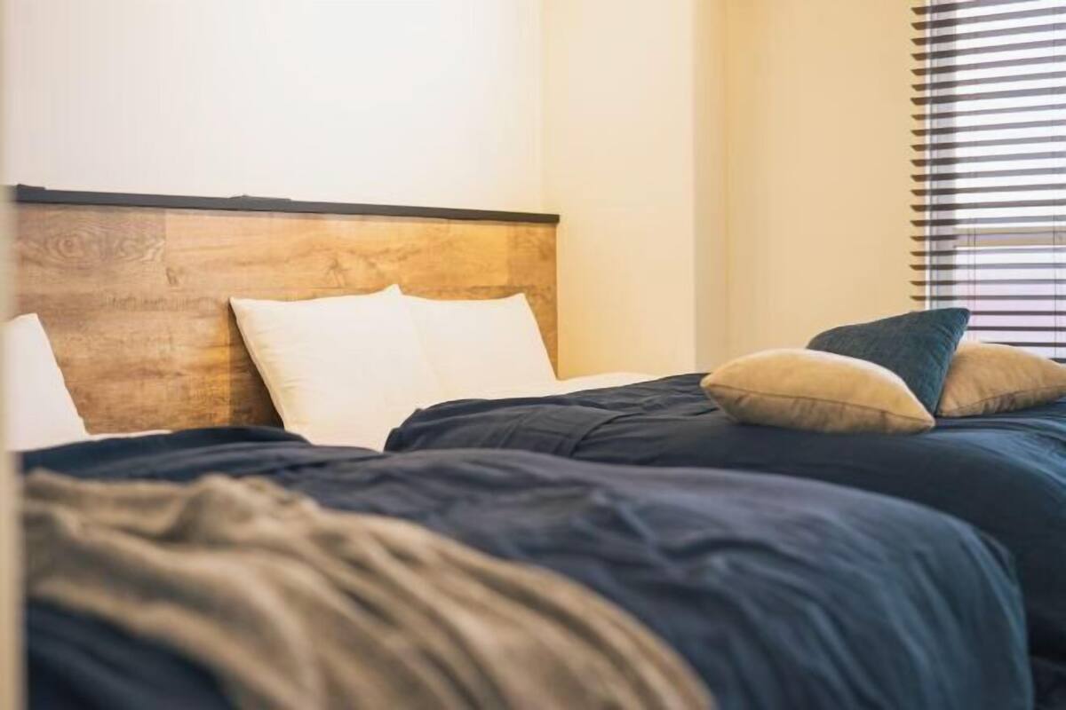 A bed with a wooden headboard, white and blue bedding, and a window with blinds.