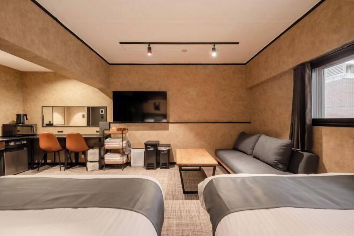 A hotel room with two beds, a desk with chairs, a TV, and a sofa.