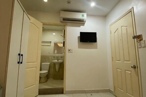 Ein Badezimmer mit Toilette, Waschbecken und Dusche. Ein Fernseher ist an der Wand montiert und über dem Waschbecken befindet sich eine Klimaanlage.