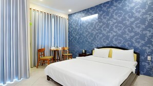 Une chambre d’hôtel avec un lit, un bureau, deux chaises et une fenêtre avec des rideaux.