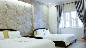Une chambre d’hôtel avec deux lits, une table de chevet, une fenêtre avec des rideaux et un mur orné d’un motif floral.