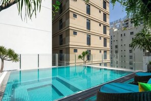 Una piscina con agua azul cristalina, rodeada por un muro blanco y un edificio de varios pisos.