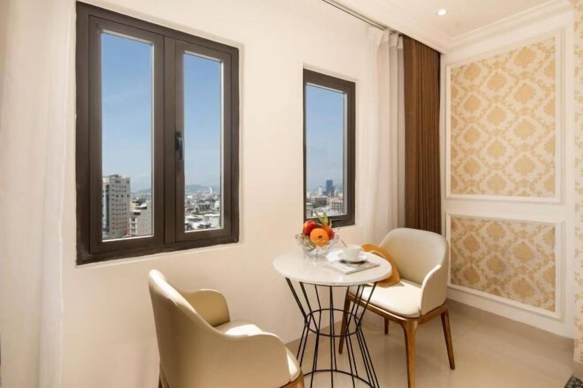 A room with two windows, a round table with chairs, and a view of the cityscape.