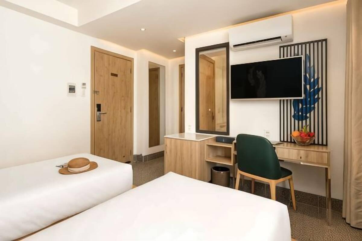 A hotel room with two beds, a desk, a chair, a TV, and a mirror.