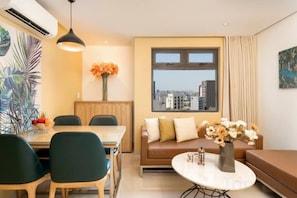 A modern living room with a dining area, a sofa with cushions, a round coffee table, and a large window with a city view.