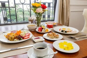 A breakfast setting with plates of food, a cup of coffee, and a vase of flowers.