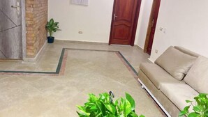 A hotel lobby with a beige sofa, a wooden door, a potted plant, and a framed artwork on the wall. - Lemon Tree & Home 2 (New Cairo City)