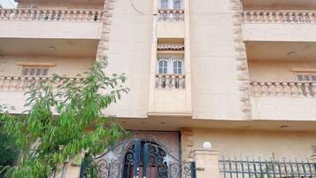 Un edificio de varios pisos con balcones, una entrada protegida por una reja y un árbol en primer plano.