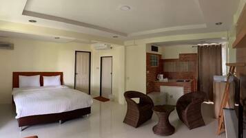 A bedroom with a bed, two chairs, a small table, a TV, and a kitchenette.
