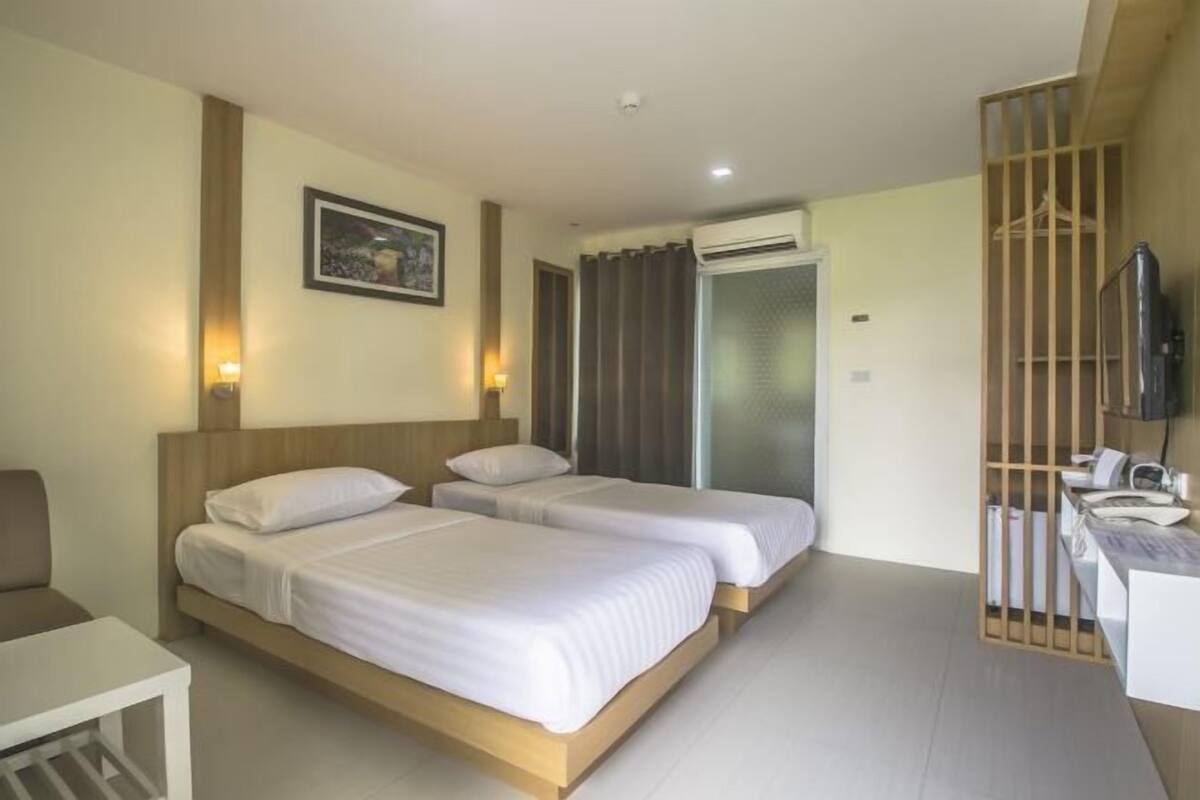 A hotel room with two beds, a desk, a chair, a TV, and an air conditioning unit.