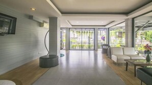 A spacious lobby with a modern design, featuring a seating area with sofas and a coffee table, a large TV mounted on the wall, and a glass door leading outside. - Petchsiri Boutique Hotel (Bangkok)