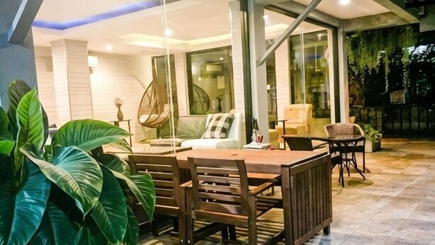 An outdoor dining area with a wooden table and chairs, surrounded by large potted plants. - Petchsiri Boutique Hotel (Bangkok)