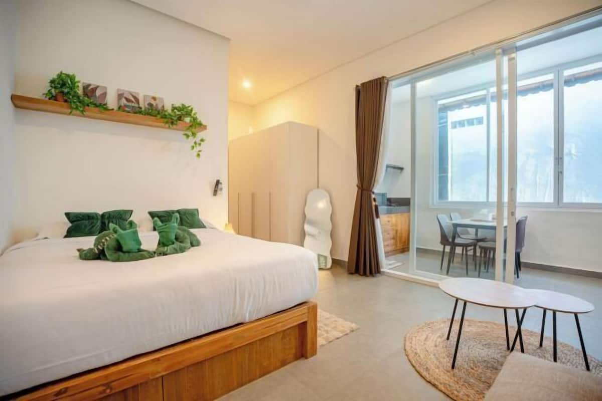 A bedroom with a bed, a bedside table, a chair, a window with curtains, and a view of the outside.