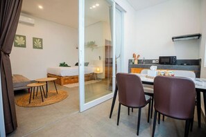 A modern hotel room with a bed, a small dining table with chairs, a microwave, and a sliding glass door leading to a balcony. - Bali Bay By Urban Haven (Bali)