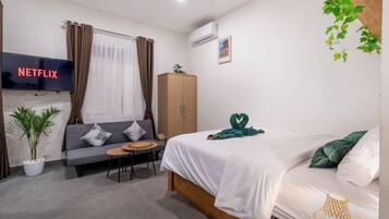 Habitación de hotel con una cama, sofá, mesita, televisión y armario.