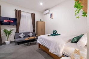 A hotel room with a bed, a sofa, a small table, a TV, and a wardrobe. - Bali Bay By Urban Haven (Bali)