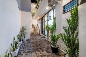 A narrow indoor corridor with a brick floor, potted plants, and a staircase leading to an upper level. - Bali Bay By Urban Haven (Bali)