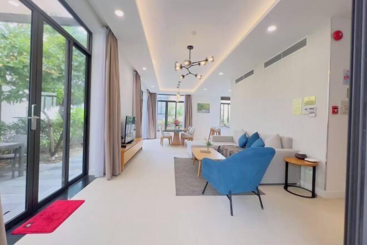 A modern living room with a blue armchair, a sofa, and a dining area with a table and chairs.