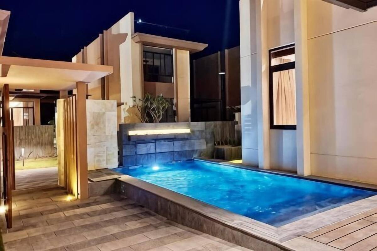 A modern outdoor swimming pool with a stone wall and a pergola.