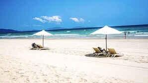 A beach with two white umbrellas and lounge chairs. - Wyndham Cam Ranh Villas (Cam Lam District)