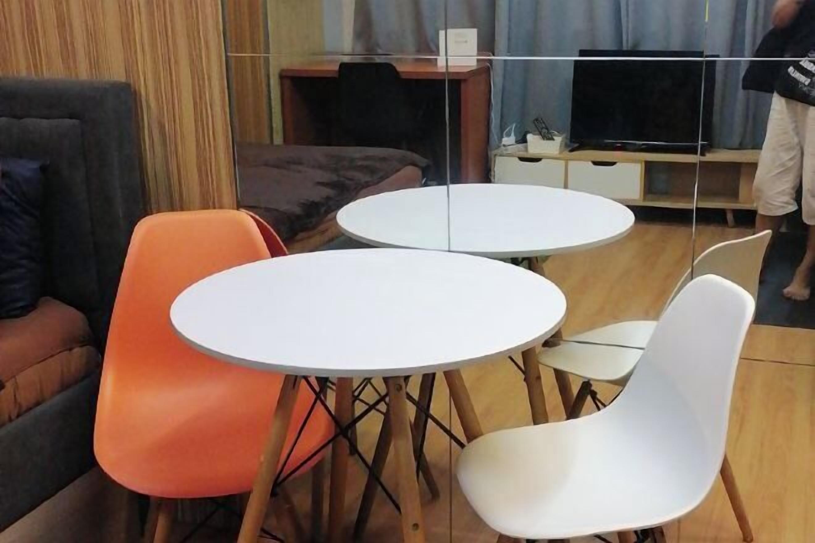 A room with two round tables and chairs, a sofa, a TV, and a wooden cabinet.