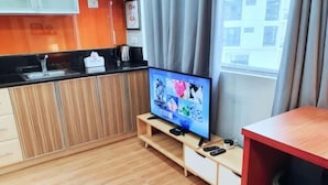 A modern kitchen with a built-in TV, wooden cabinets, and a window with curtains. - Maison at the Hill at Morgan Suites Mckinley Hill BGC Taguig (Taguig)