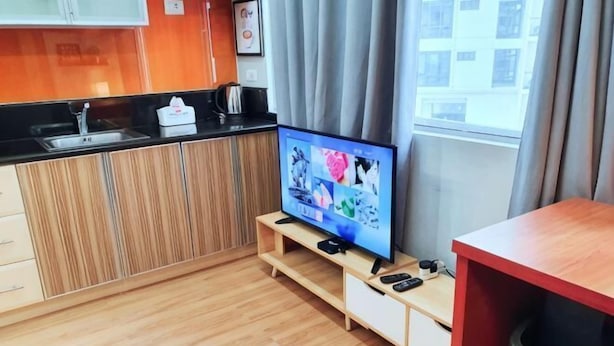 A modern kitchen with a built-in TV, wooden cabinets, and a window with curtains. - Maison at the Hill at Morgan Suites Mckinley Hill BGC Taguig (Taguig)