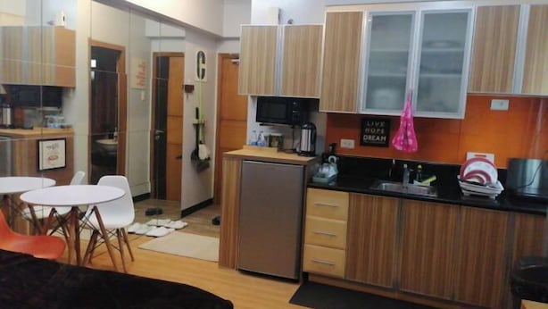 A compact kitchen with wooden cabinets, a small refrigerator, and a microwave. There are white chairs and a small dining table. - Maison at the Hill at Morgan Suites Mckinley Hill BGC Taguig (Taguig)