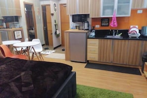 Een ruimtelijk ingerichte leefruimte met een kitchenette, een eethoek en een bed.
