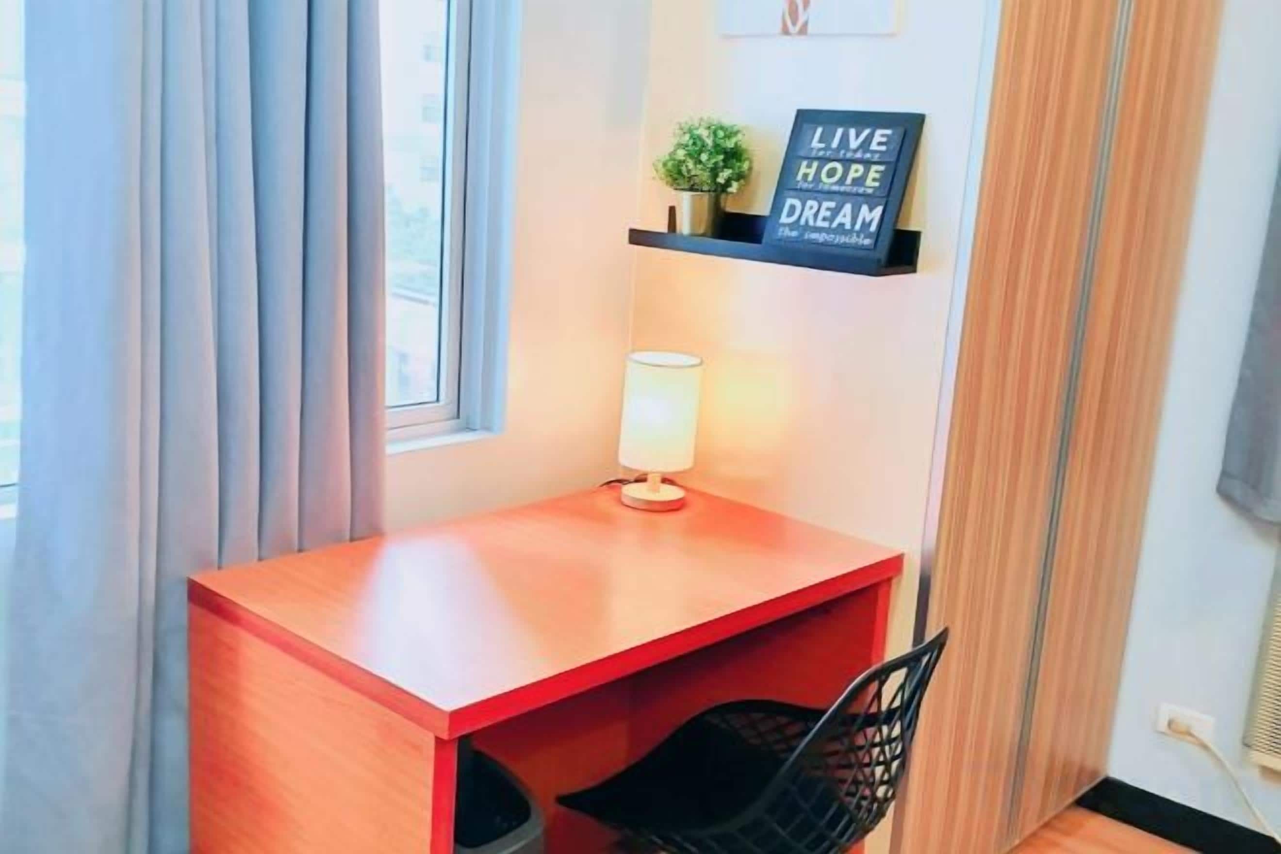 Ett litet skrivbord i trä med en lampa, en svart stol och en hylla med en motiverande skylt.