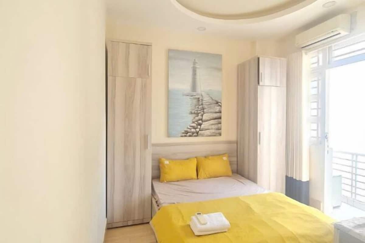 A hotel room with a bed, a painting of a lighthouse, and a balcony with a railing.