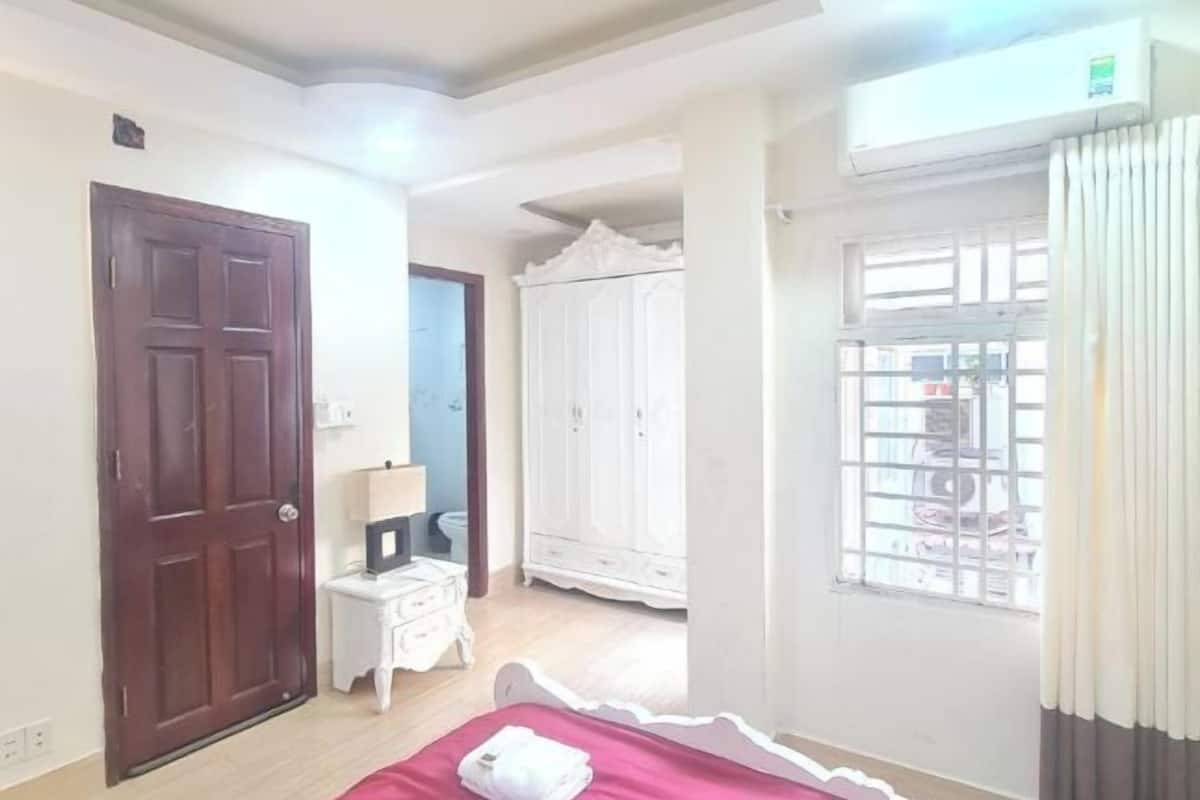 A bedroom with a bed, a wardrobe, a small bedside table, and a window with curtains.
