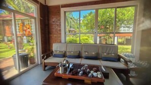A room with a large window, a sofa with cushions, and a tray with various items on a table. - MANJU SEMPORNA RESORT (Semporna)