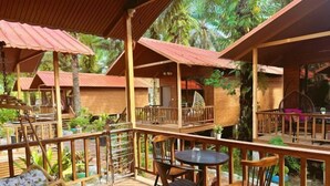 A wooden deck with outdoor seating, surrounded by lush greenery and palm trees. - MANJU SEMPORNA RESORT (Semporna)