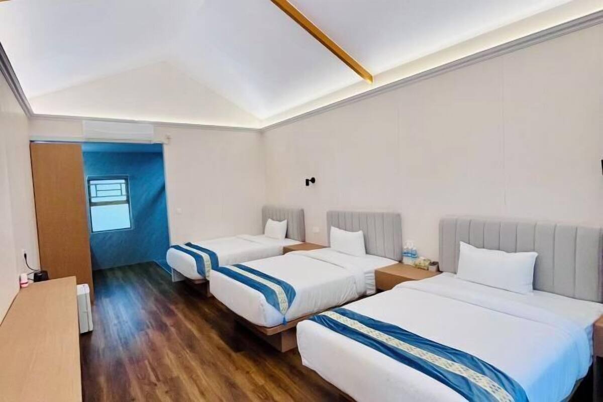 A hotel room with three beds, wooden flooring, and a small desk.