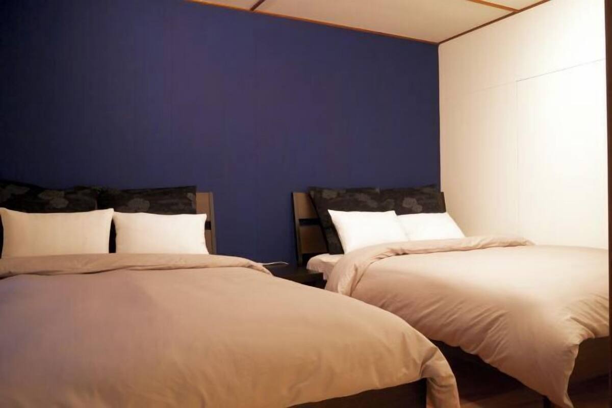 A hotel room with two beds, a blue accent wall, and a white wall.