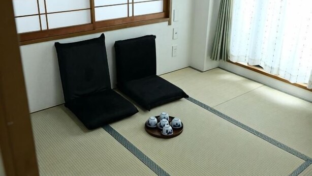 Een kamer met tatami vloerbedekking, zwarte kussens, een dienblad met theeservies en een shoji scherm.