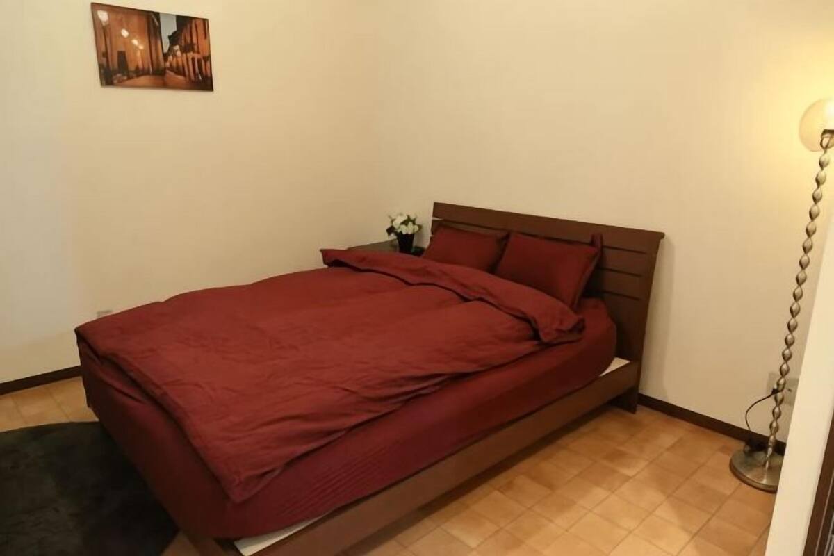 A single bed with a wooden headboard, a small bedside table with a plant, and a wall-mounted picture.