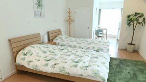 Een slaapkamer met twee bedden, een groen vloerkleed, een plant in pot en een deur naar een balkon.