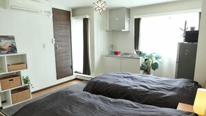 Een slaapkamer met twee bedden, een kleine kitchenette, een plant en een raam.