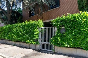 Zona residencial cerrada con un edificio de ladrillo, un camino de hormigón y arbustos verdes.