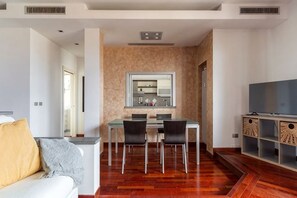 Una sala de estar moderna con sofá, una mesa de comedor con sillas, televisión y una cocina al fondo.