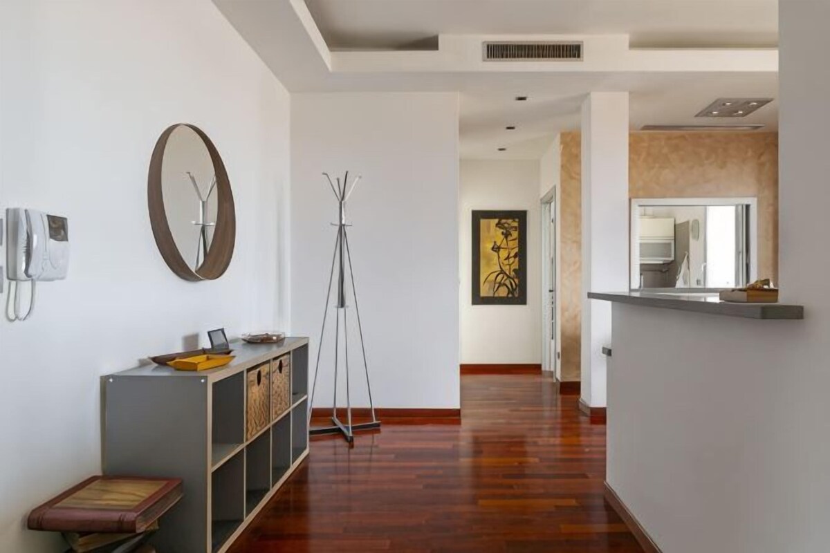 A hallway with a wooden floor, a standing lamp, a coat rack, and a framed artwork on the wall.