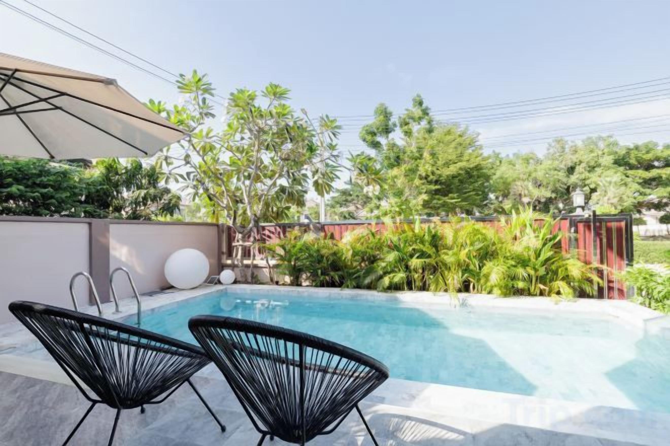 A swimming pool with two black chairs, surrounded by greenery and a red fence.