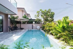 A modern swimming pool with a clear blue water surface, surrounded by lush greenery and a patio area with a table and chairs. - Pattaya Holiday Villa (Venice Single Villa)【8 minutes drive to floating market + swimming pool】 (Pattaya)