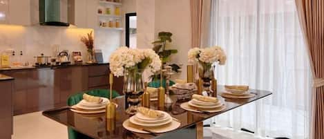 A modern dining area with a glass table, green chairs, and white flowers.
